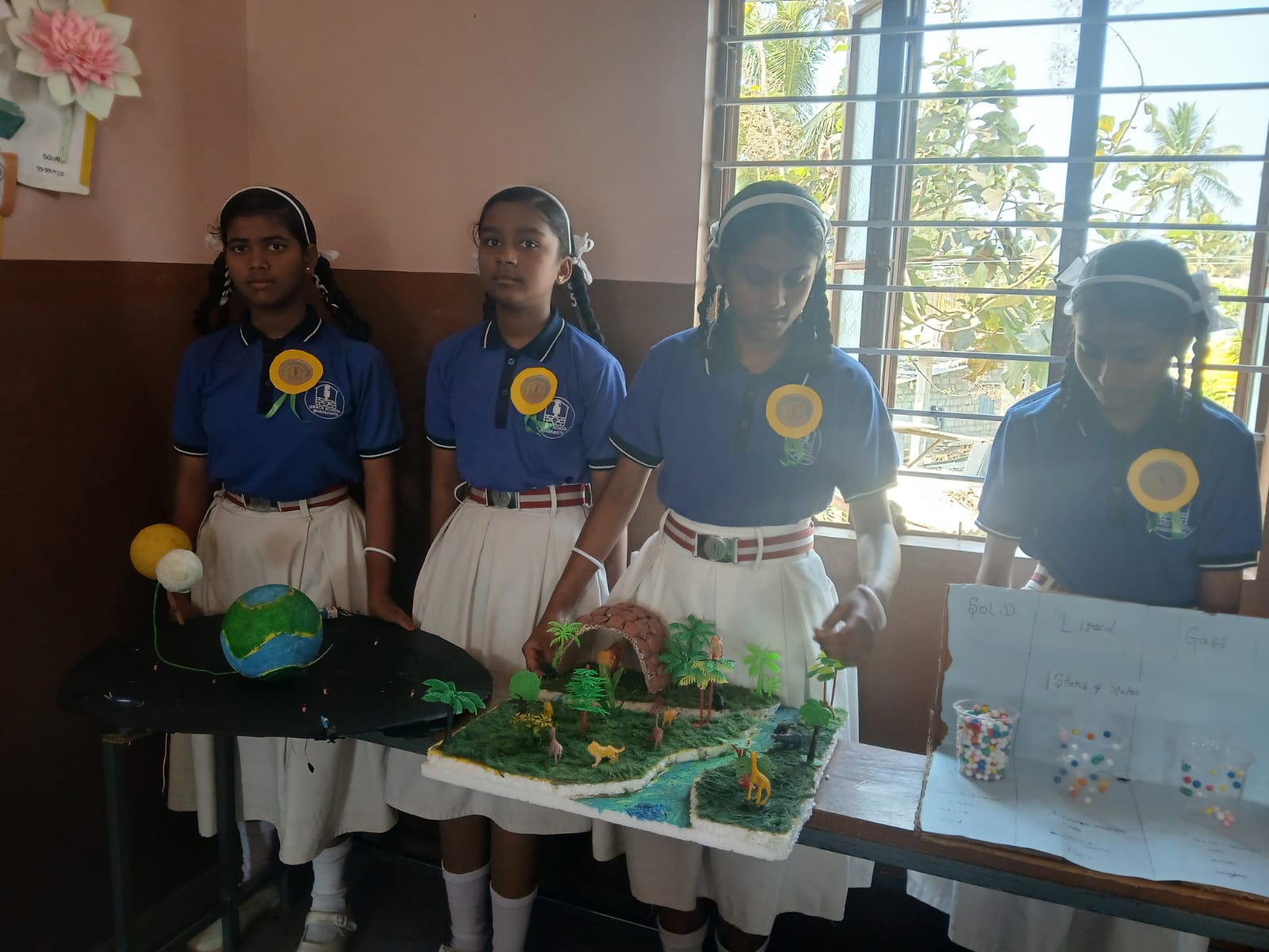 Four girls display models representing the solar system, wildlife habitat, and states of matter.